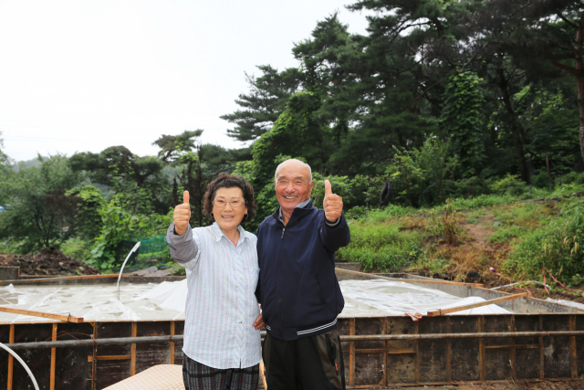 화재로 집을 잃은 이대명·조명자 부부가 스틸하우스가 지어질 집터를 배경으로 기쁨을 전하고 있다. 포스코 제공.