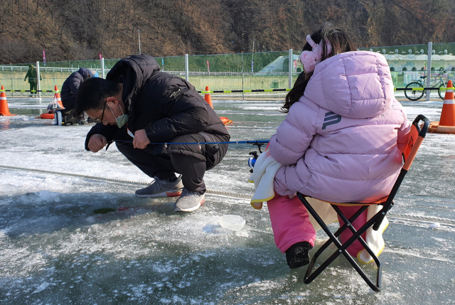 딸과 함께 산천어 축제장을 찾은 한 시민이 얼음구멍속으로 낚싯줄을 드리우고 있다.