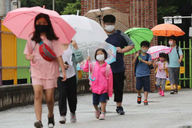 광주·전남지역에 비가 내린 18일 오전 광주 북구 오치초등학교에서 학생들과 병설유치원생들이 마스크를 쓰고 코로나19 예방 발열체크를 하기 위해 줄지어 이동하고 있다. 연합뉴스