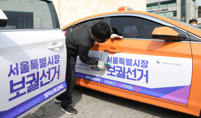 지난 3월 3일 서울시선관위 관계자들이 성북구 대왕기업 택시차고지에서 서울시장 보궐선거 홍보물을 붙이고 있다. 연합뉴스