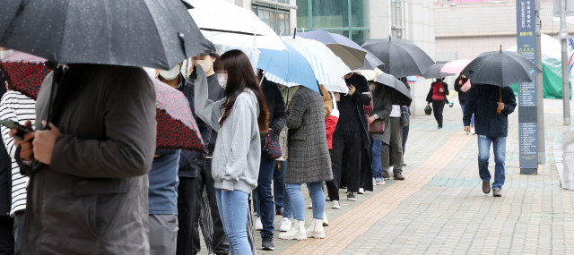 12일 오후 서울 중랑구 보건소에 마련된 코로나19 임시선별진료소를 찾은 시민들이 우산을 쓰고 순서를 기다리고 있다. 연합뉴스