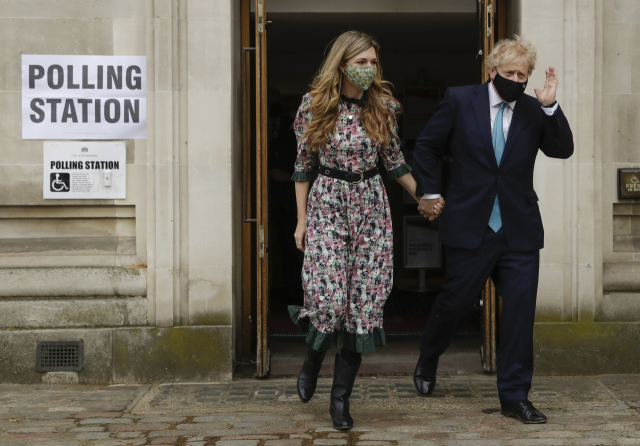 보리스 존슨 영국 총리가 6일(현지시간) 런던의 한 지방선거 투표소에서 약혼녀 캐리 시먼즈와 함께 투표한 뒤 나오면서 손을 흔들고 있다. 영국 전역에서 치러지는 이번 지방선거는 2019년 총선 이후 치러지는 가장 큰 규모의 선거다. 연합뉴스