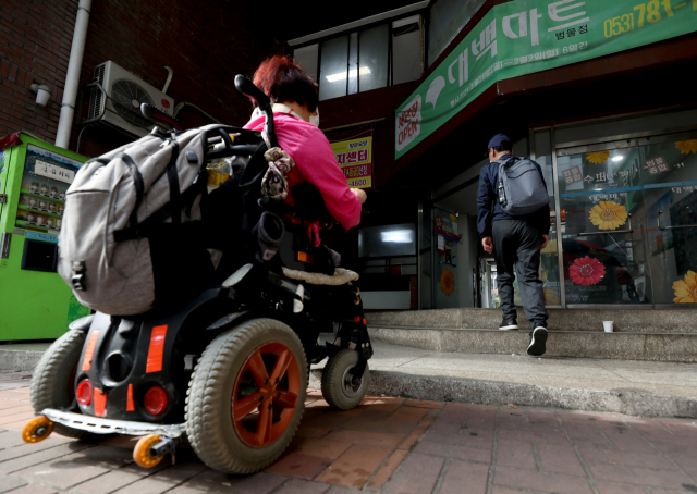 13일 오후 대구 수성구 용지아파트 상가 건물 출입구에 휠체어 장애인을 위한 경사로가 설치돼 있지 않아 전동 휠체어를 탄 한 장애인이 계단 앞에 멈춰 서 있다. 안성완 기자 asw0727@imaeil.com