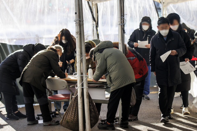 질병관리청에서 관리하는 코로나19 선별검사 시스템 접속에 문제가 생긴 18일 서울역 광장에 마련된 임시 선별검사소에서 시민들이 접수를 위해 수기로 관련 설문지를 작성하고 있다. 연합뉴스