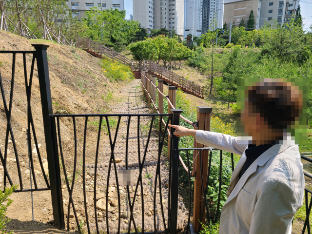 구미 호반베르디움 아파트 입주민이 학교와 도시숲을 가로막는 철제 울타리를 손으로 가리키고 있다.