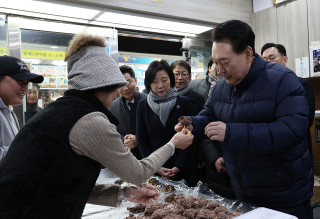 윤석열 대통령이 25일 경기도 의정부시 의정부제일시장을 찾아 떡 가게에서 상인이 건넨 떡을 맛보고 있다. 연합뉴스