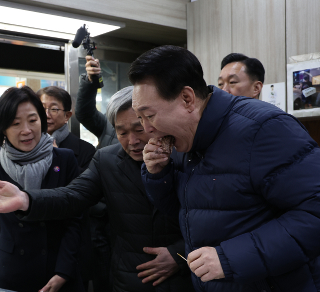 윤석열 대통령이 25일 경기도 의정부시 의정부제일시장을 찾아 떡 가게에서 상인이 건넨 떡을 맛보고 있다. 연합뉴스