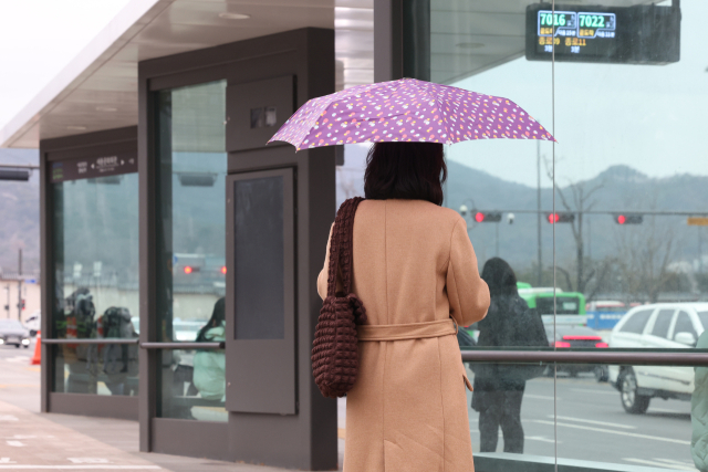 서울 종로구 광화문광장에서 한 시민이 우산을 쓰고 버스를 기다리고 있다. 연합뉴스