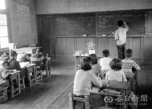 1969년 6월 지산국민학교 범물분교 조경환(33) 선생님이 4,5,6학년이 함께 배우는 교실에서 칠판을 나눠 산수와 국어 복식수업을 하고 있다. 왼쪽 벽에 1968년 12월 5일 발표된 국민교육헌장이 붙어 있다. 사진=매일아카이빙센터