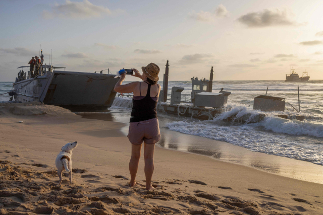 25일(현지시간) 이스라엘 해안 도시 아슈도드의 한 해변에서 미군 함정이 좌초된 모습을 한 여성이 사진으로 찍고 있다. 미군은 가자 지구에 해상 지원을 위해 임시 부두를 건설하는 과정에서 4척의 함정이 거친 바다에서 좌초됐다고 밝혔다. AFP 연합뉴스