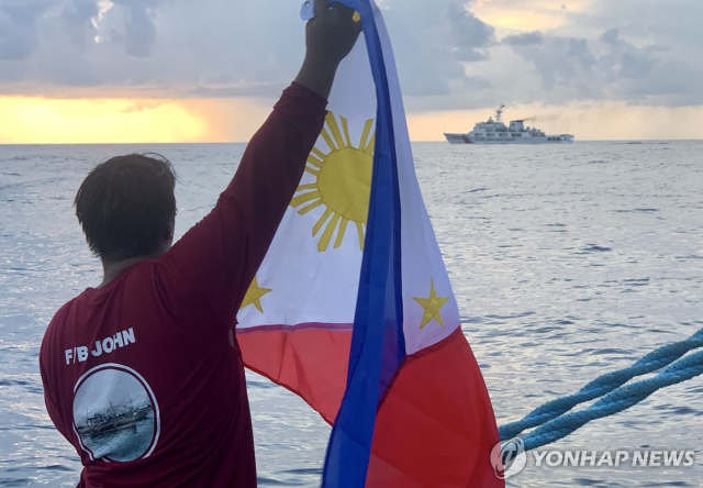 지난 5월 16일(현지시간) 남중국해에서 스카버러 암초(중국명 황옌다오·黃岩島)로 향하던 필리핀 어선을 중국 해경선이 막아서자 어민이 필리핀 국기를 들어 보이고 있다. 2024.6.15 [EPA 자료사진]