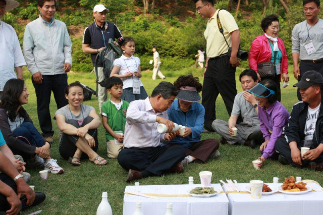 2008년 6월 6일 경남 김해시 봉하마을의 모내기 체험행사를 함께 한 32가족 자원봉사자 100여명과 새참 시간을 갖는 노무현 전 대통령과 권양숙 여사 내외(노무현 전 대통령이 권양숙 여사에게 막걸리를 따라주는 모습). 노무현 사료관