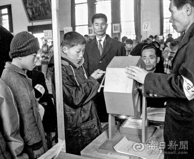 1970년 2월 4일 대구여중에서 열린 남자 중학교 첫 무시험 진학 추첨이 6학년 어린이가 추첨기를 돌리고 있다. 추첨은 왼쪽으로 두 번 돌려 은행알을 섞고 오른쪽으로 한번 돌리면 자신이 진학할 학교 번호가 적힌 은행알이 나오는 방식이었다. 사진=매일아카이빙센터