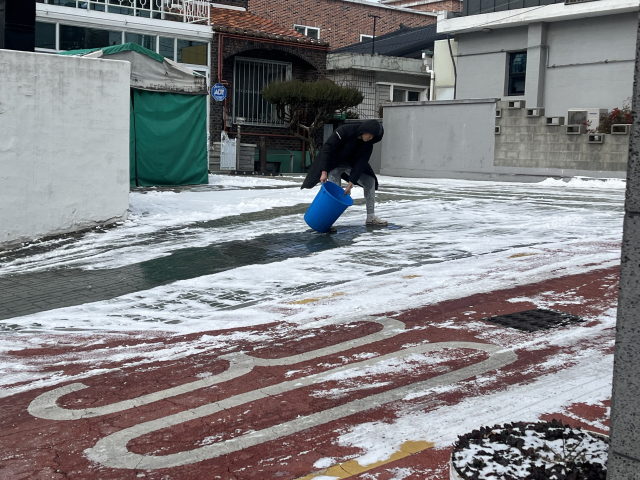 눈이 내린 지난 7일 대구 도심 이면 도로에서 한 주민이 눈을 녹이기 위해 뜨거운 물을 붓고 있다. 정두나 기자