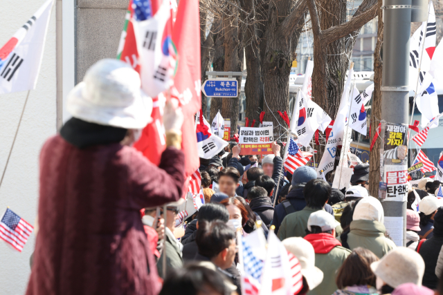 윤석열 대통령 탄핵심판 사건이 헌법재판소에 접수된 지 95일째인 19일 서울 종로구 헌재 건너편에서 윤 대통령 지지자가 탄핵 각하를 촉구하는 가운데 보행자와 대통령 지지자가 뒤섞여 있다. 연합뉴스